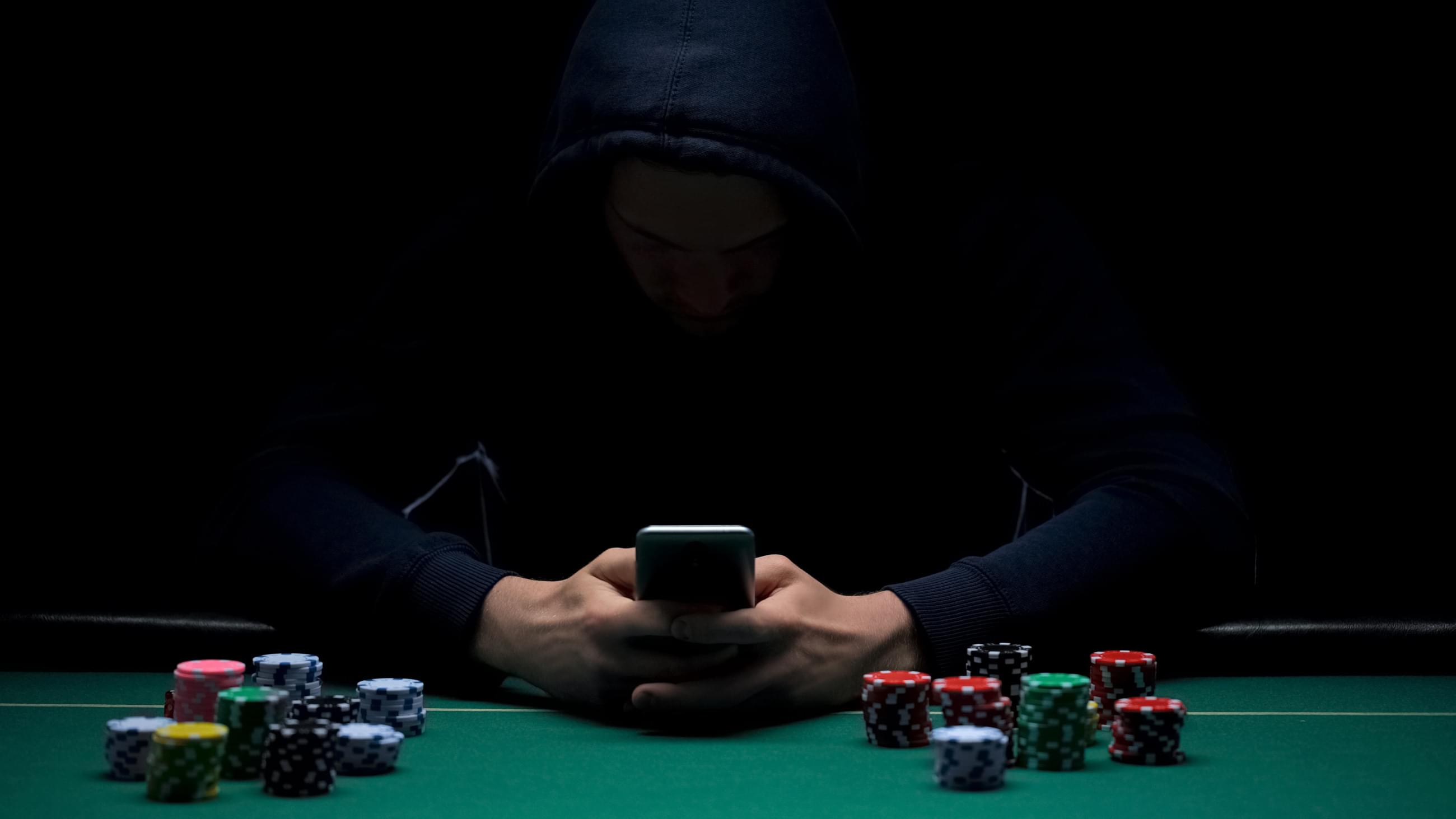muž v kapuci sedící s mobilním telefonem u pokerového stolu s žetony