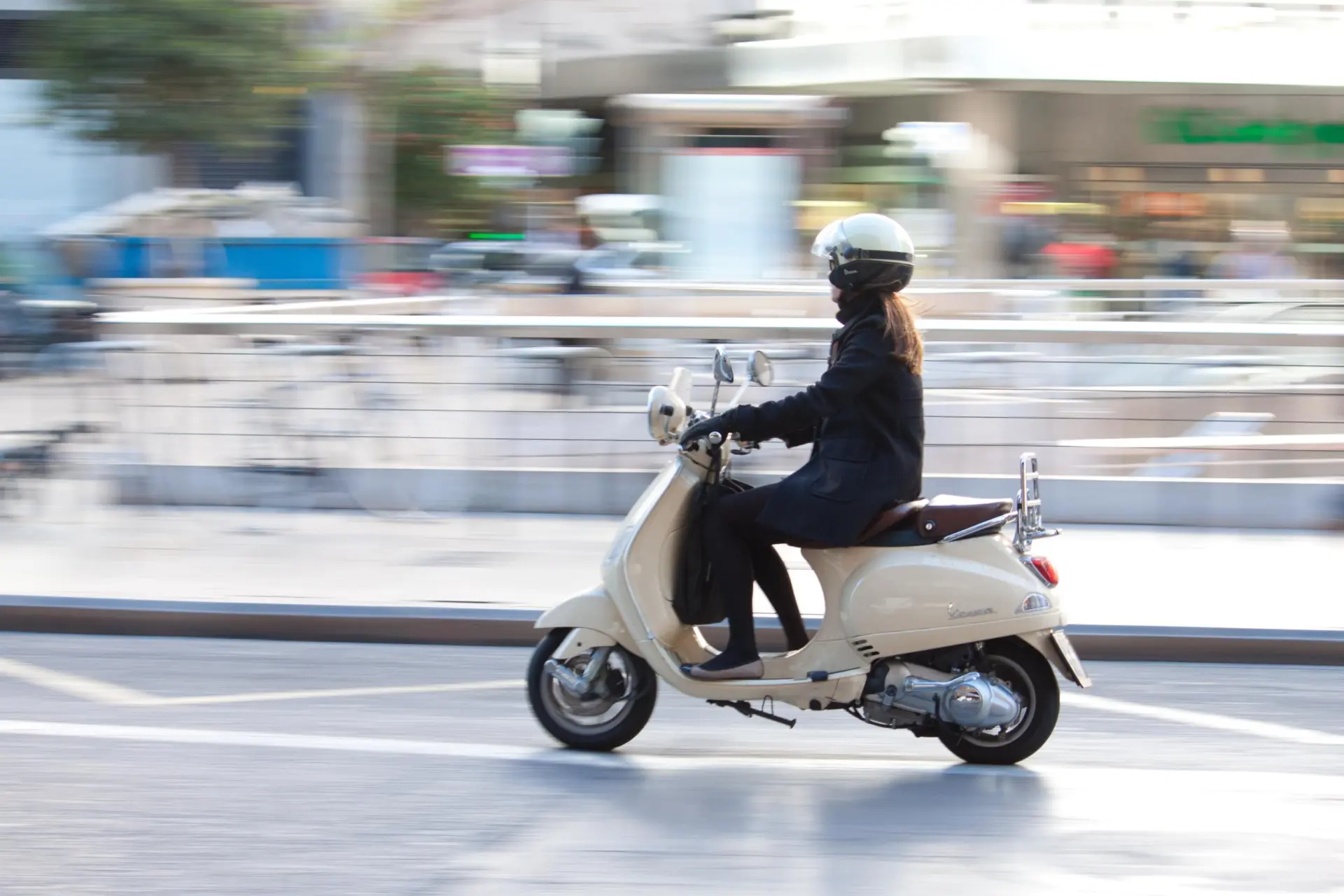 žena jedoucí na bílém skútru Vespa italskou ulicí